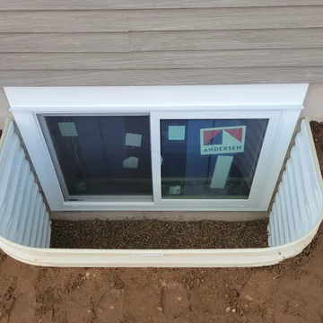 Double Andersen glider egress window with corrugated metal well installed on gray siding exterior