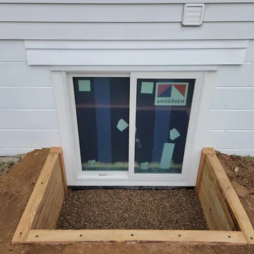 Double timber egress window well with wide Andersen glider window on gray siding exterior
